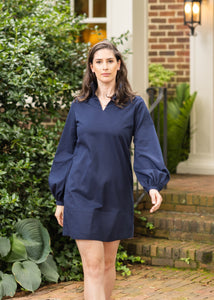 Woman in a blue dress walking on a brick path in front of a house.