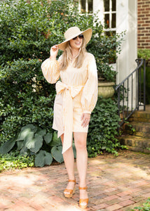Woman in a white dress and hat standing in front of a brick house.