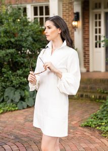 Woman in a white dress standing on a brick path in front of a house.