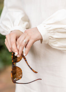 Woman wearing a cream dress holding sunglasses
