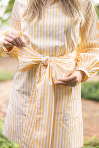 Woman wearing a yellow and white striped dress with a bow detail, standing outdoors.