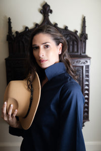 Woman holding a beige hat against a decorative wooden headboard.