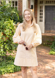 Woman in a yellow dress standing on a brick path in front of a house.